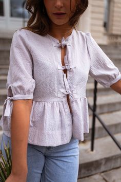 Lilac gingham patterned slight-balloon short sleeve blouse that features a cute bow to tie in the front, as well as bow detailing on the sleeves. This blouse has a flowy-slightly loose fit and dies not offer lining. The perfect unique and trendy spring-summer wardrobe staple. Our models also wear the White Baptiste Jeans and the Light Blue Maddie Jeans. Sizes: S / M / L S: Length 20.87 in - Width 18.11 in M: Length 21.26 in - Width 18.90 in L: Length 21.65 in - Width 19.69 in 100% Cotton Washing: Handwash and cold water Spring Tie Waist Tie Neck Top, Spring Tops With Tie Waist And Tie Neck, Cotton Puff Sleeve Blouse With Tie Sleeves, Cotton Blouse With Tie Sleeves And Puff Sleeve, Chic Gingham V-neck Blouse, Casual Tops With Tie Puff Sleeves, Casual Blouse With Puff Tie Sleeves, Casual Tops With Tie And Puff Sleeves, Casual Blouse With Tie Waist For Brunch