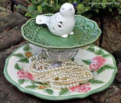 a white bird figurine sitting on top of a green and white plate with pearls