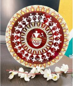 a red and white plate sitting on top of a wooden table next to some flowers