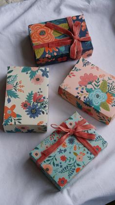 four wrapped gift boxes on a bed with ribbon tied around the top and one open