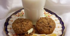 two muffins on a plate next to a glass of milk and an orange slice