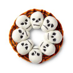 six crocheted skulls are arranged in a circle on an orange and white background