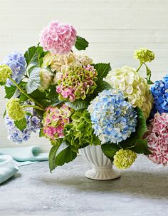 a vase filled with lots of colorful flowers on top of a white tablecloth next to blue and green napkins