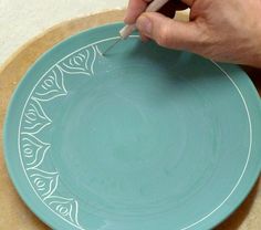 a person is using a sharpie to draw designs on a blue plate with white trim