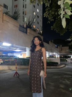 a woman standing in the middle of an empty parking lot at night with buildings behind her