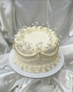 a three layer cake with white frosting flowers and pearls on the top is sitting on a plate