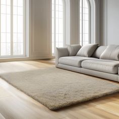 a white couch sitting on top of a hard wood floor next to a large window