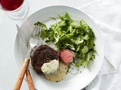 a white plate topped with steak and greens next to a fork, knife and glass of wine