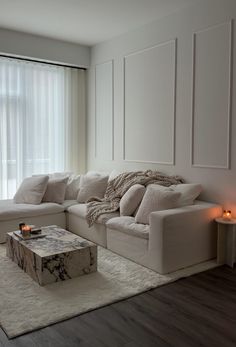 a living room with white furniture and candles on the coffee table in front of a large window