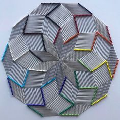 a circular object made out of metal rods and colored pencils on a white surface