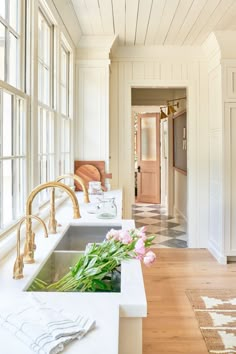 a kitchen with white walls and wooden floors has flowers on the counter in front of the sink