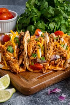 shredded chicken tacos on a cutting board with cilantro, limes and tomatoes