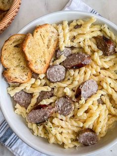 a white bowl filled with pasta and sausage next to two slices of toasted bread