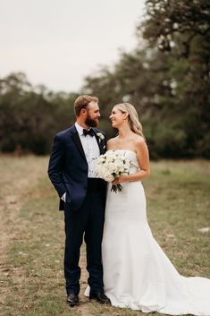 a bride and groom standing together in the grass