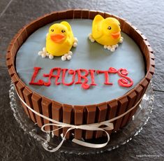 two yellow rubber ducks sitting on top of a chocolate cake that says laurits