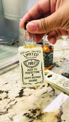 a person is holding a miniature bottle of birthday liquor in front of a counter top