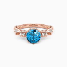 a rose gold ring with blue topazte and diamonds on the sides, set against a white background