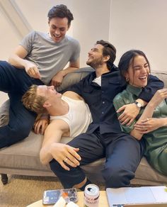 three men and one woman are sitting on a couch laughing at the same person who is holding his arm around him