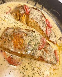 two fish fillets are cooking in a skillet with tomatoes and herbs on top