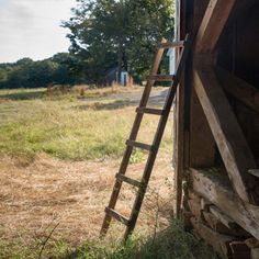 an old wooden ladder leaning against the side of a building in front of a field