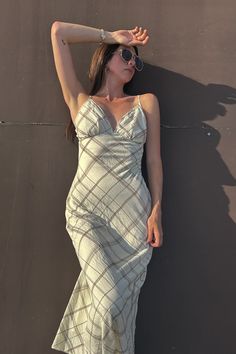 a woman in a white dress leaning against a wall with her hand on her head