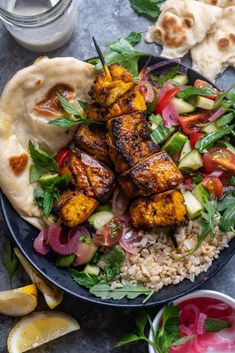 a blue plate topped with chicken and veggies on top of rice next to pita bread