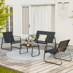 three chairs and a table sitting on a wooden deck next to a white building with sliding glass doors