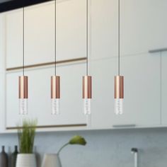 three copper and white lights hanging from a kitchen ceiling over a sink with a potted plant in the foreground