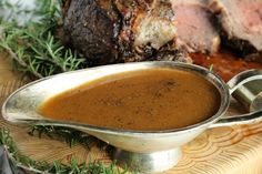 a bowl filled with gravy sitting on top of a wooden table next to meat