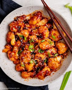 a white bowl filled with chicken and chopsticks on top of a table next to green onions