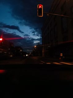 a red traffic light sitting above a street next to a tall building at night with dark clouds in the sky