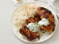 a plate with chicken, rice and sauce on it next to a glass of wine