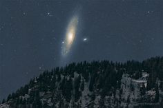 two very large objects in the sky above some trees and snow covered mountains at night