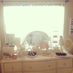 a dresser with various items on it in front of a large mirror and windowsill