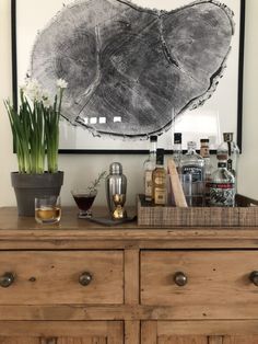 a wooden dresser topped with lots of bottles and glasses next to a vase filled with flowers