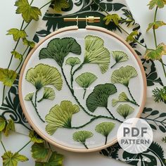 a cross stitch pattern with green leaves on white fabric and gold thread in the middle