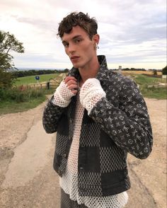 a man standing on a dirt road with his hands in his pockets and wearing a jacket