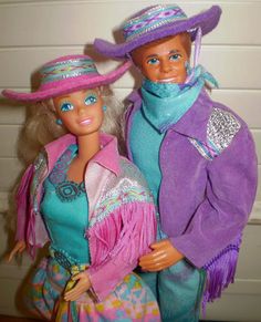 two barbie dolls dressed in colorful clothes and hats, one is holding the other's hand