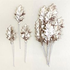 three silver leaves are placed on sticks against a white wall and one is upside down