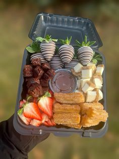 a person holding a tray with strawberries, chocolate covered strawberries and other foods