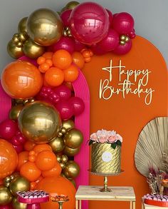 an orange and pink birthday party with balloons on the wall, cake table and decorations