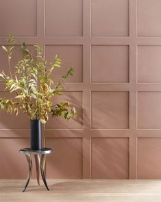 a plant in a vase sitting on a table next to a wall with pink tiles