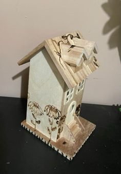 a small wooden house with flowers painted on the roof and windows is sitting on a table