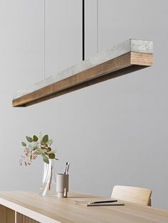 a wooden table topped with a vase filled with flowers and greenery next to a light fixture