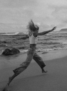 a woman running on the beach with her hair blowing in the wind and water behind her