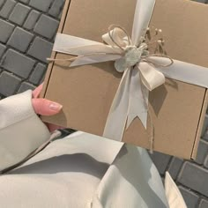 a woman is holding a brown box with a white ribbon on it and she has her hand wrapped around the gift