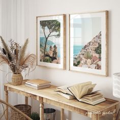 two framed pictures hang on the wall above a wooden table with books and vases