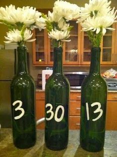 three green bottles with white flowers in them sitting on a kitchen counter next to an oven