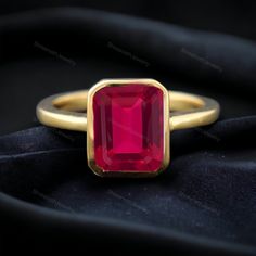 a gold ring with a large red stone on the top and bottom, sitting on a black cloth