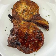 two pieces of meat on a white plate with parsley sprinkled around it